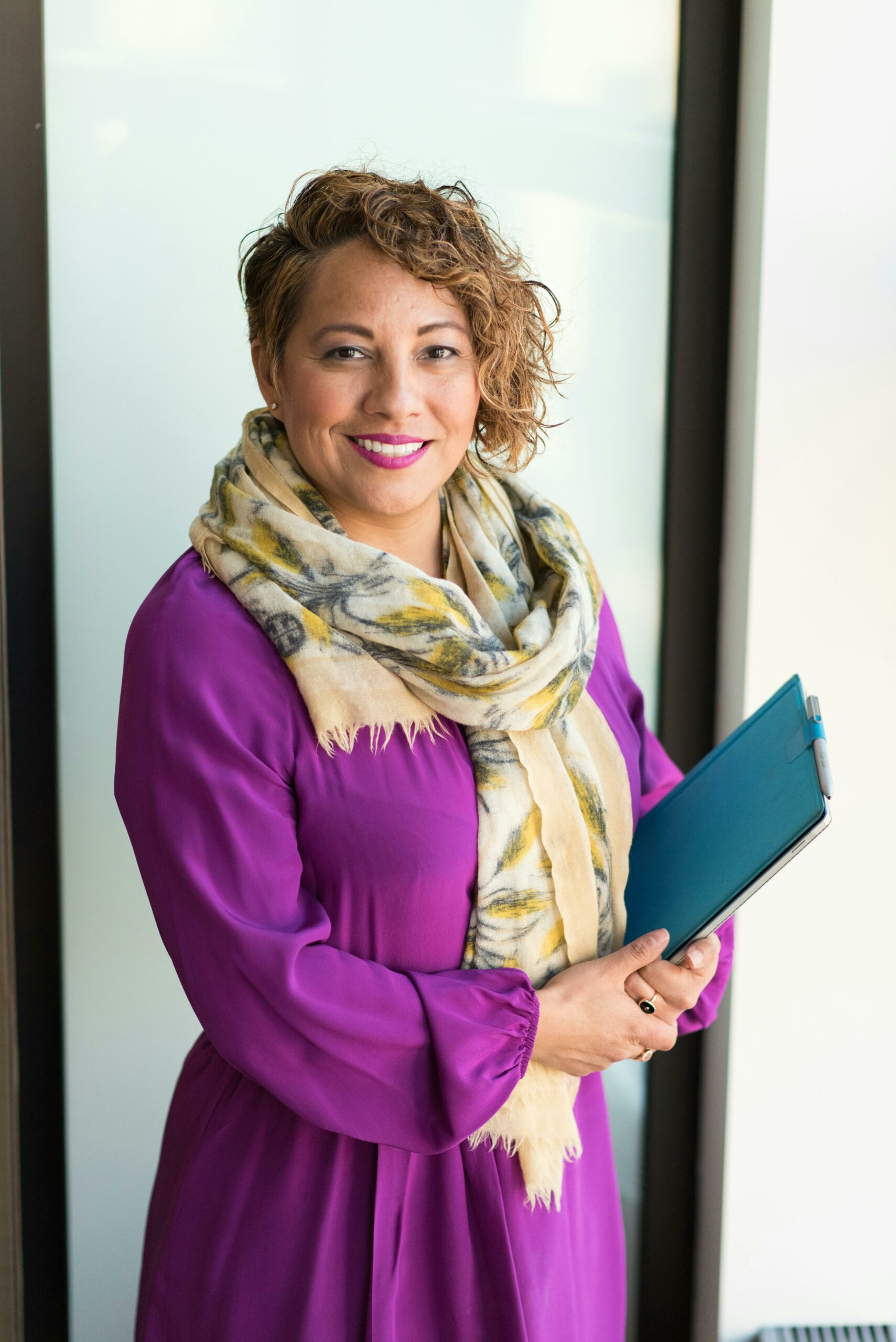 Home Smiling woman in a purple dress and scarf holding a tablet indoors.